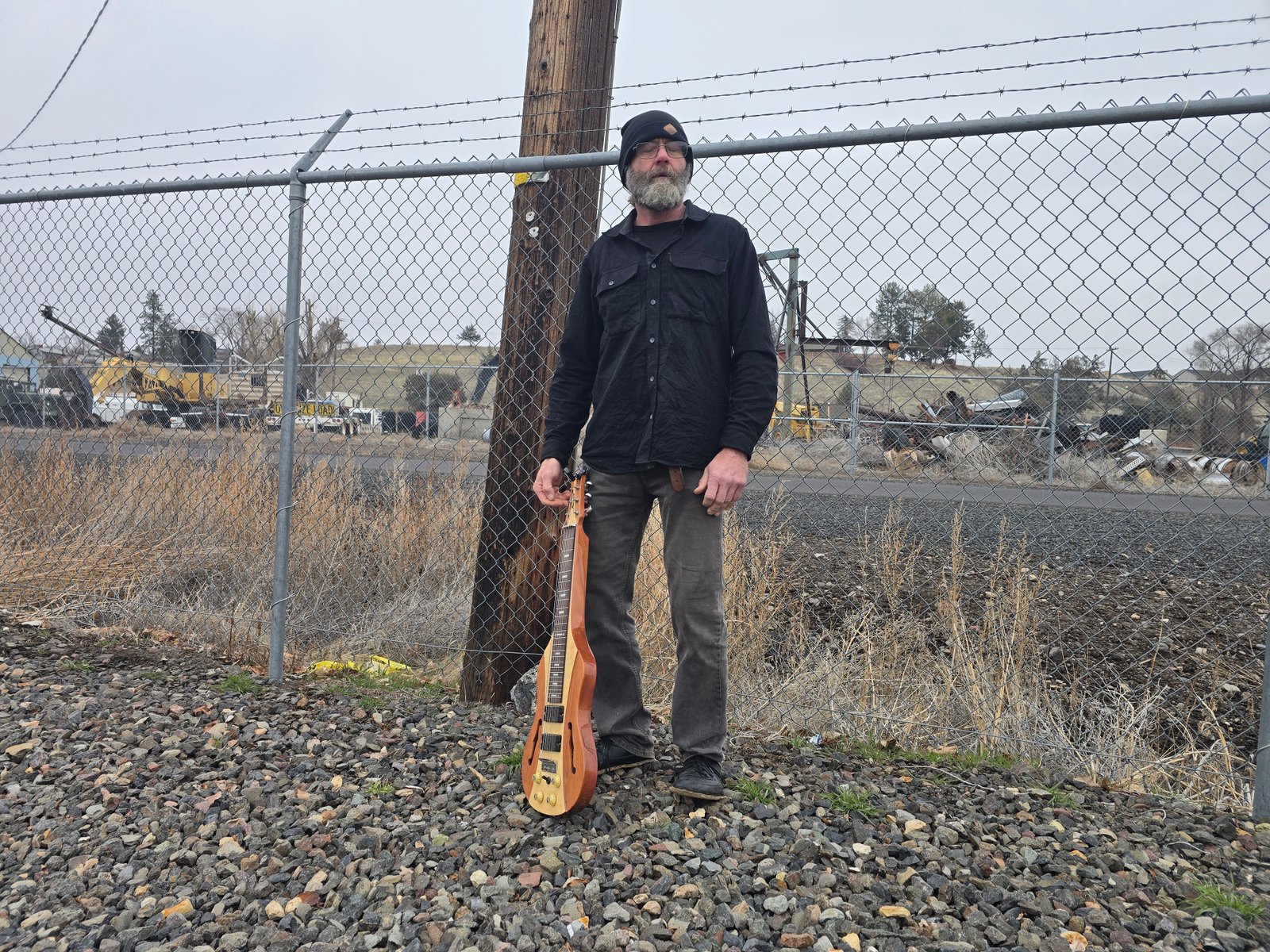 Band member with bass against a chain-link fence at dusk